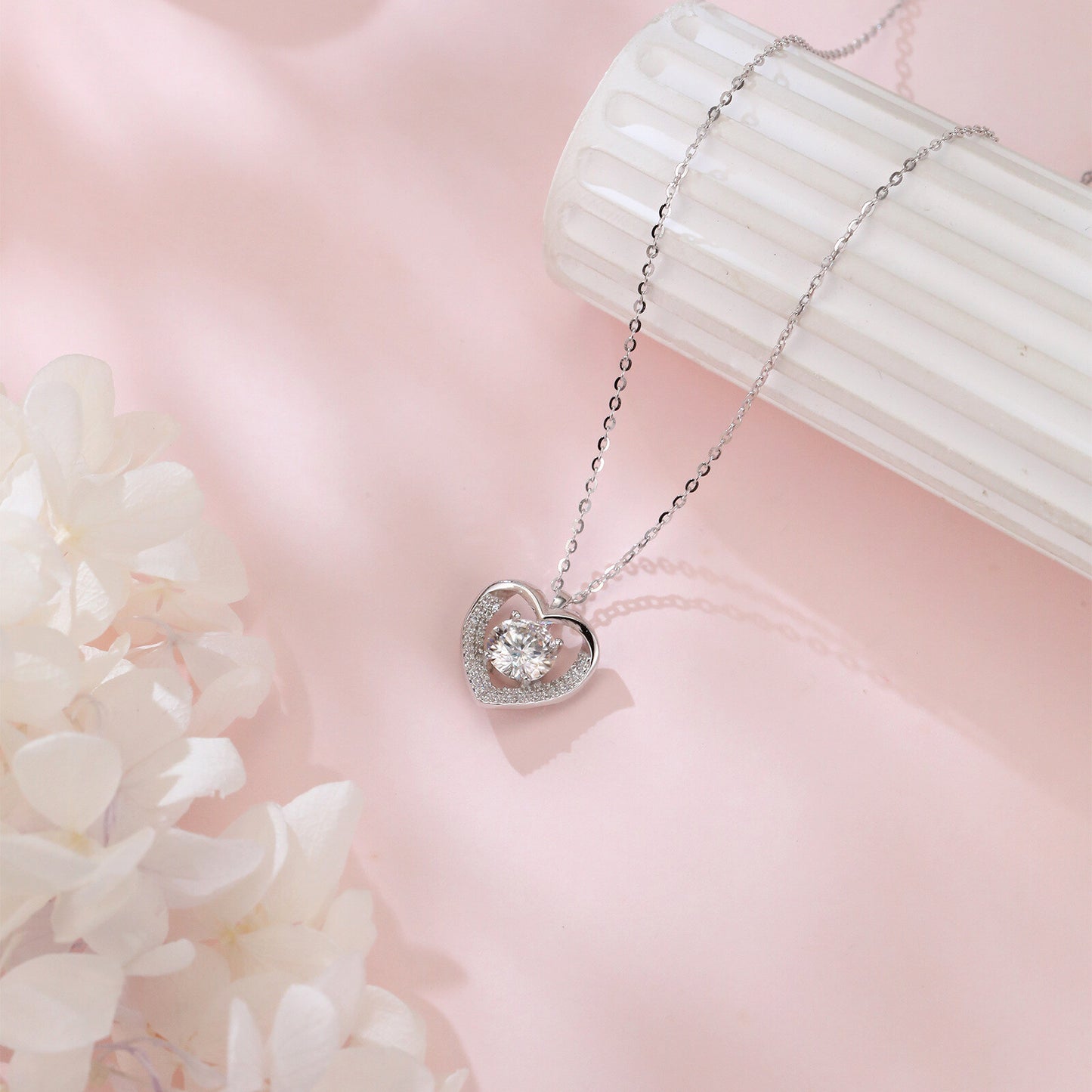 Heart-shaped silver necklace with a diamond pendant on a pink background