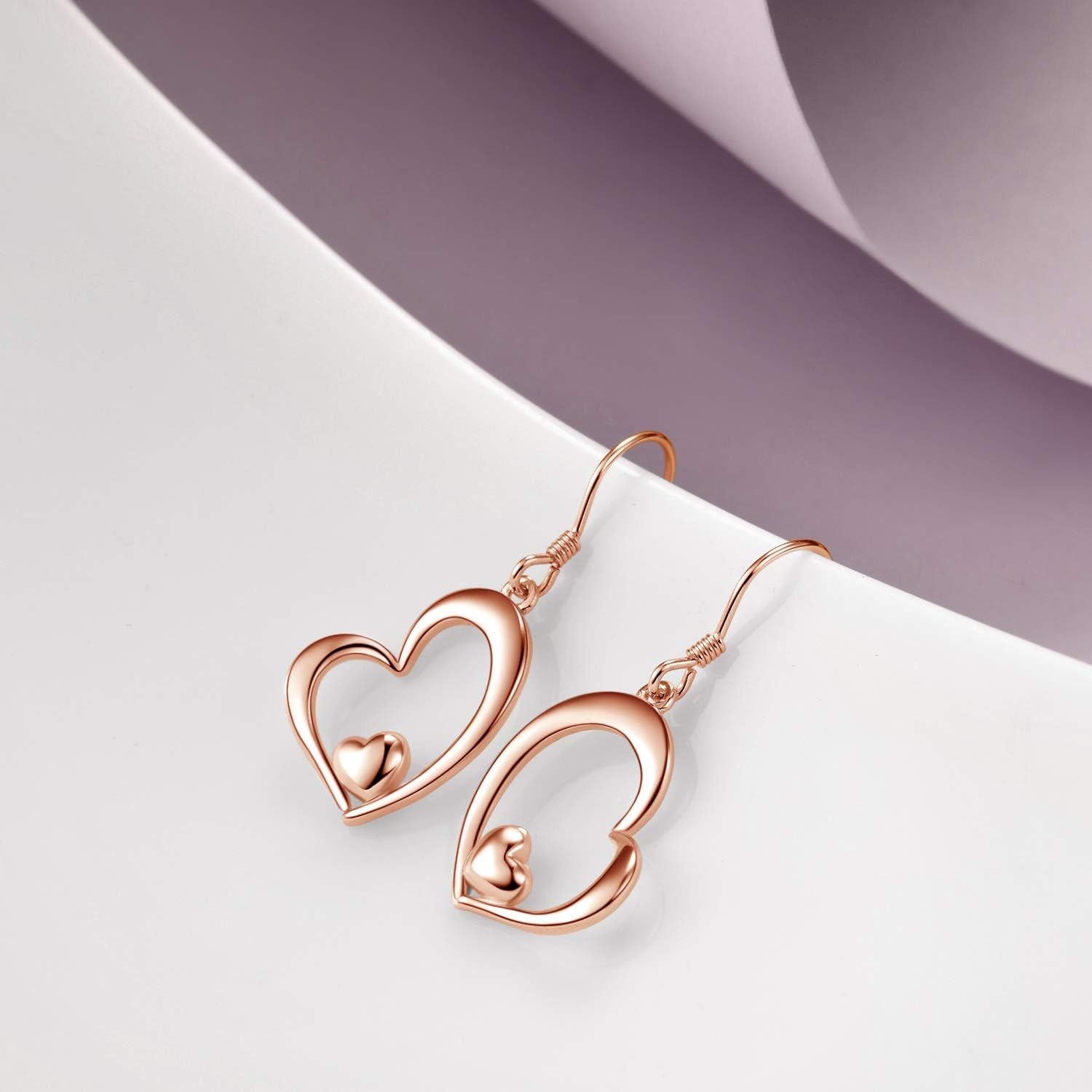 Rose gold heart-shaped earrings on a white surface with a purple background