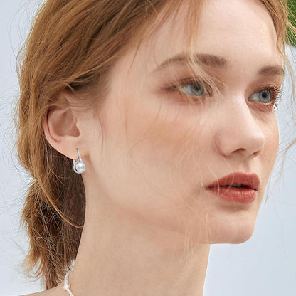 Close-up of a woman wearing a silver earring with a pearl on a light background
