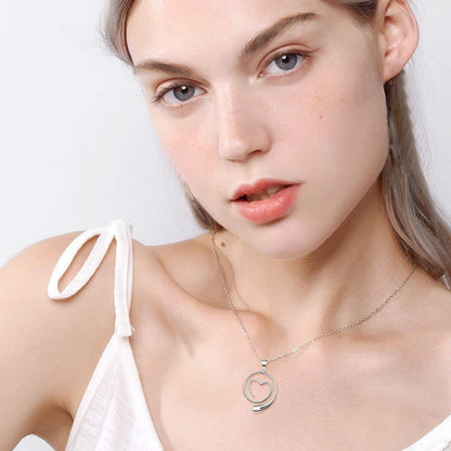 Woman wearing a silver necklace with a heart pendant on a white background