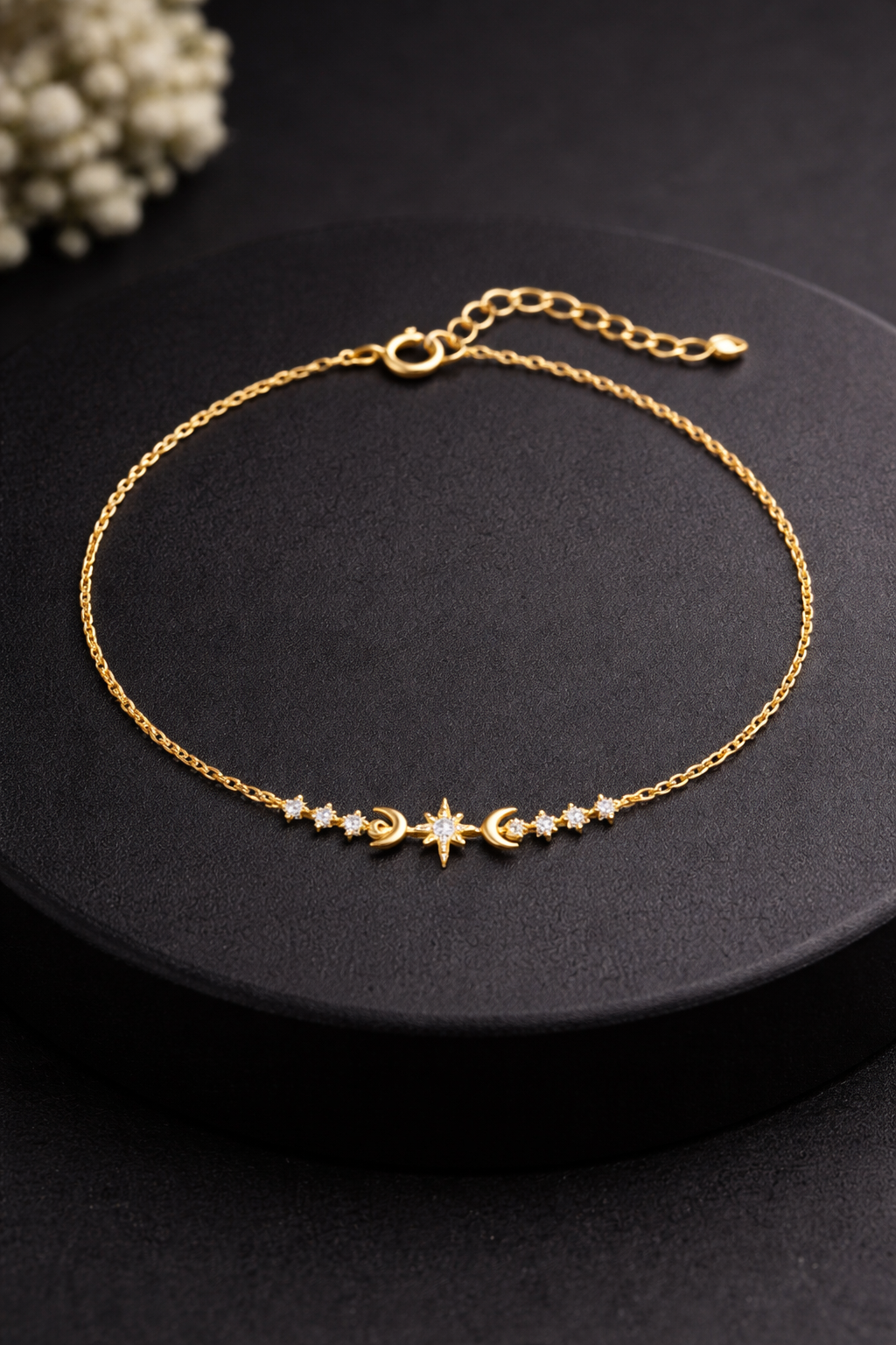 Gold bracelet with star and moon charms on a black surface