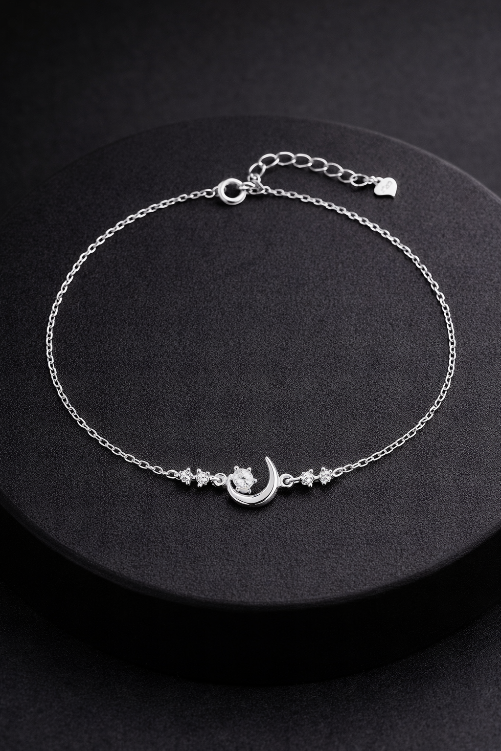 Silver anklet with a moon and star design on a black background