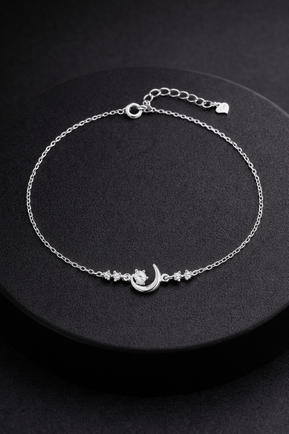 Silver anklet with a moon and star design on a black background