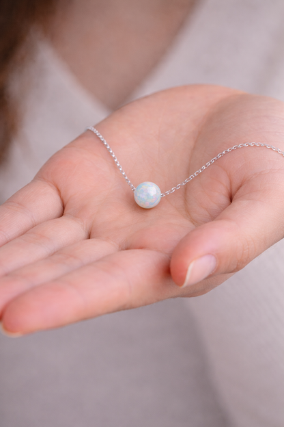 Silver necklace with a pendant held in a hand against a neutral background