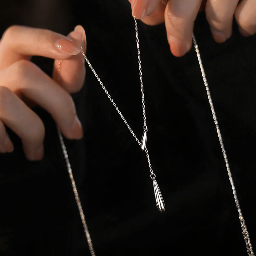 Close-up of a silver necklace with a tassel pendant held by hands against a black background