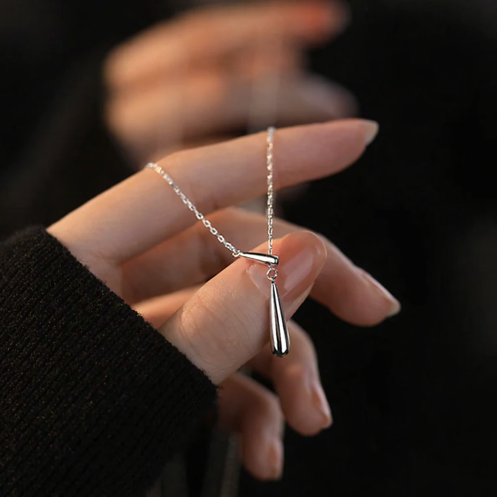 Silver necklace with a pendant held by a hand against a dark background