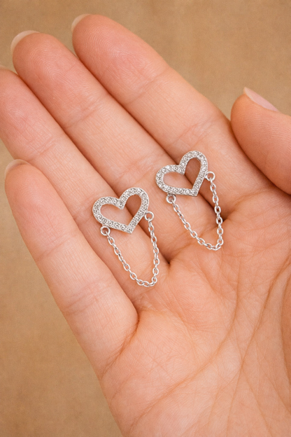 Silver heart-shaped earrings held in a hand against a beige background
