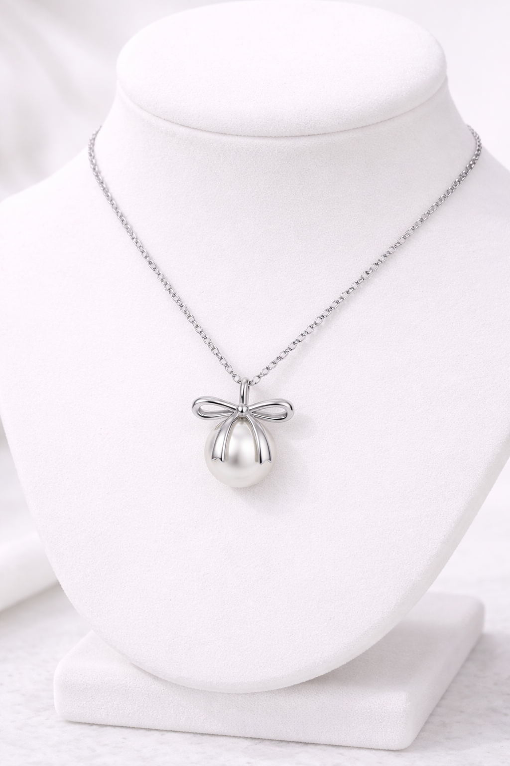 Silver necklace with a bow pendant on a white mannequin bust.