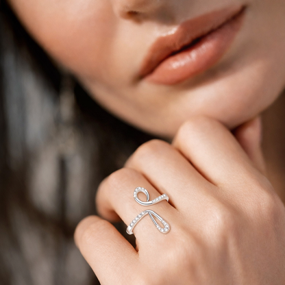 Close-up of a hand wearing a silver ring with a bow design, against a blurred background.