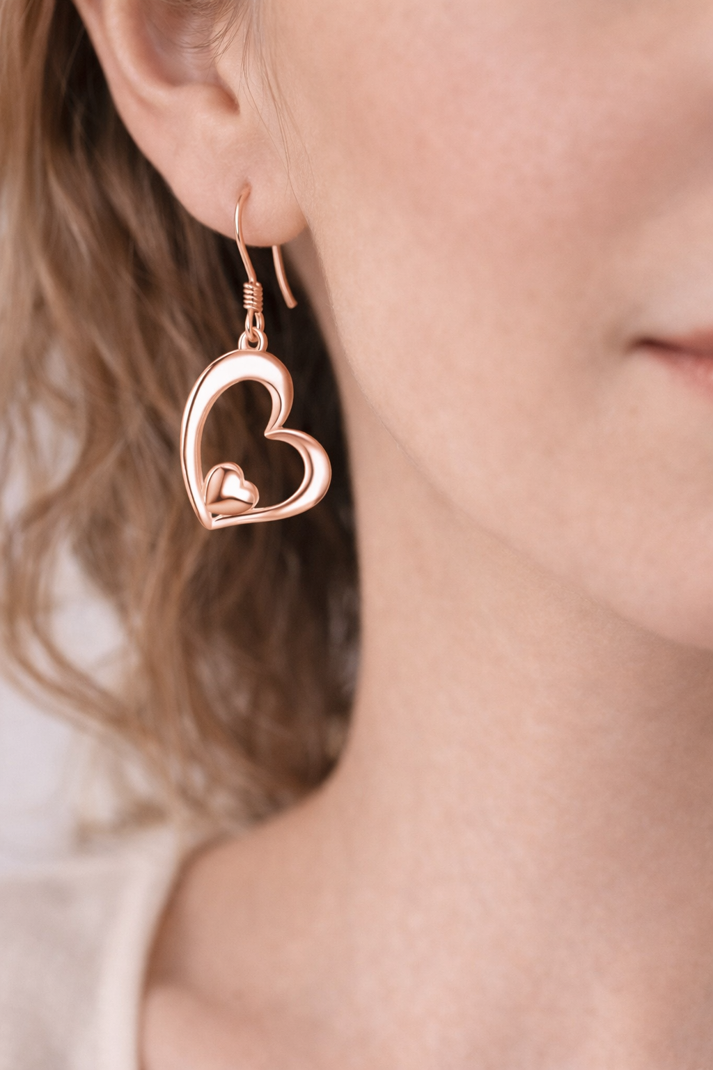 Rose gold heart-shaped earrings worn by a person with blurred background