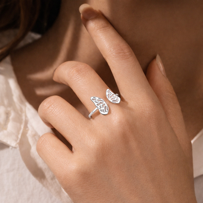 Silver ring with leaf design on a person's finger against a neutral background
