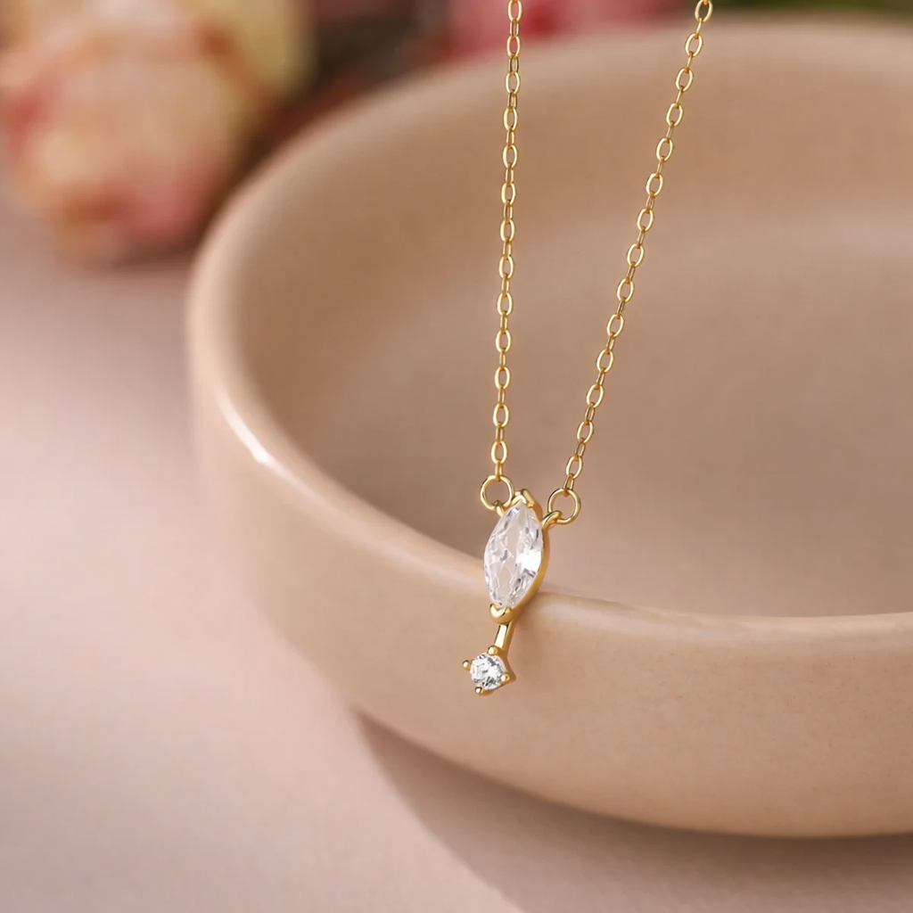 Gold necklace with a clear pendant on a pink ceramic dish