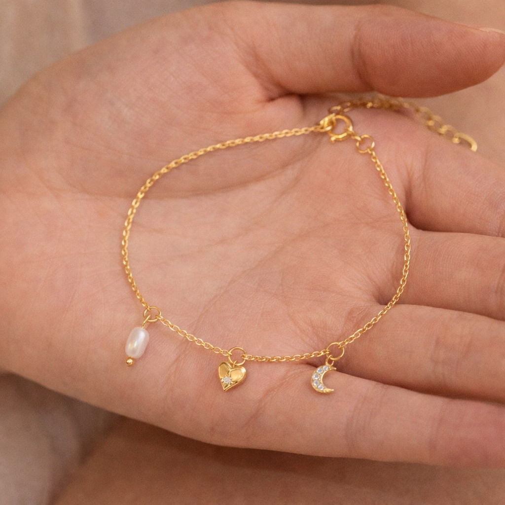 Gold bracelet with charms on a hand against a neutral background