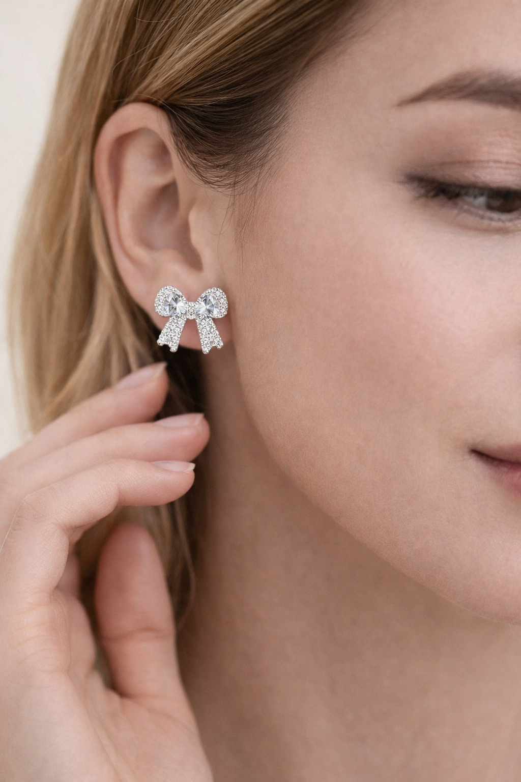 Close-up of a person wearing a bow-shaped earring with a hand adjusting it.