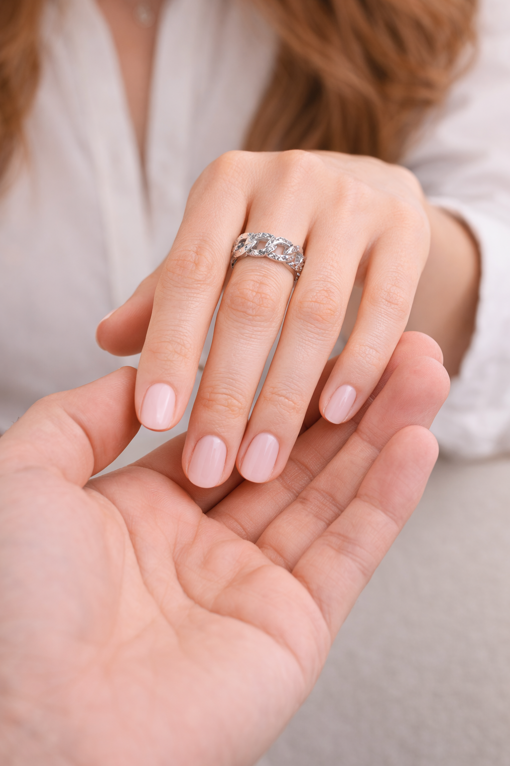 Close-up of a hand wearing a silver ring with another hand holding it, on a neutral background.