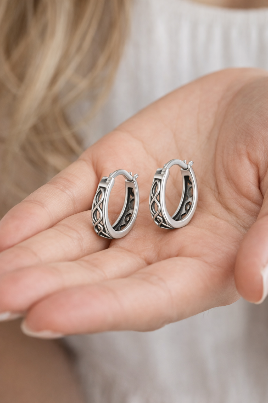 Silver hoop earrings held in a hand against a neutral background