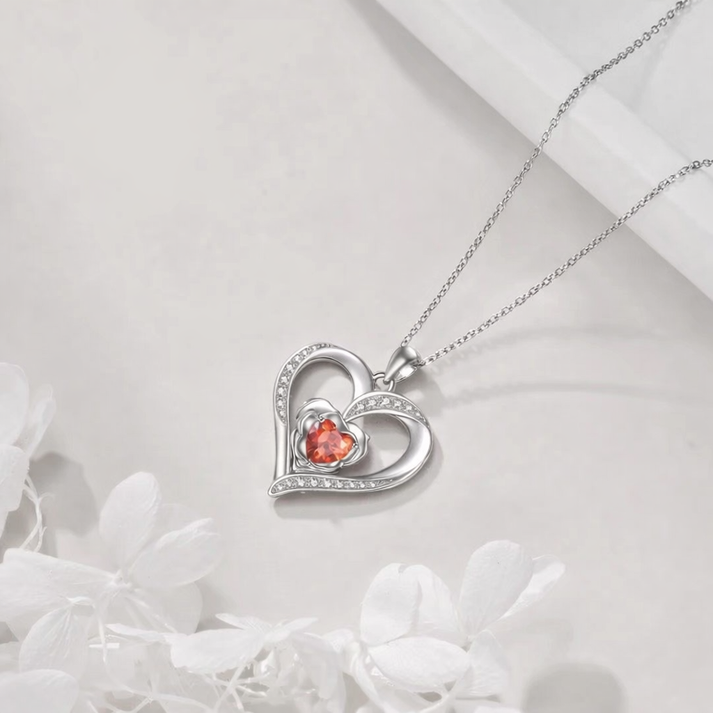 Heart-shaped silver pendant with a red gemstone on a white background