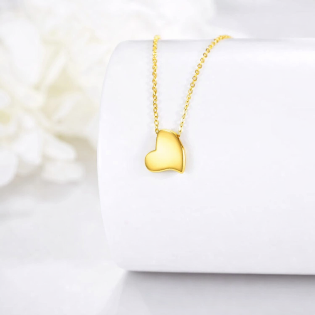Gold heart-shaped necklace on a white box with a soft floral background