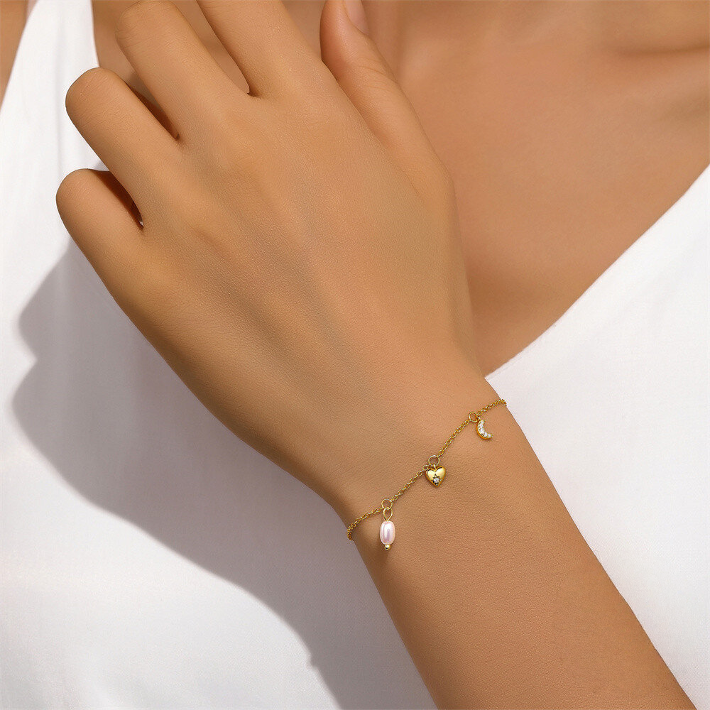 Gold bracelet with heart and moon charm on a wrist against a white background