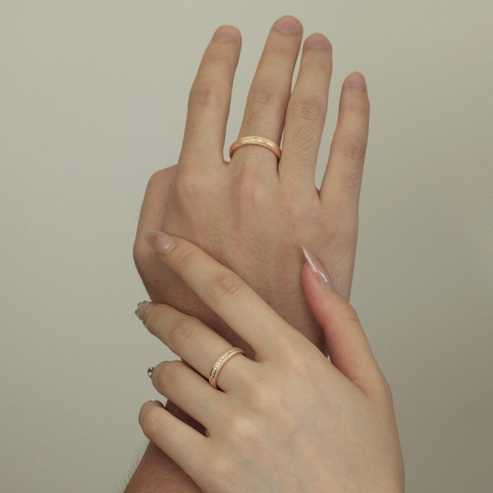 Two hands with gold rings on a plain background