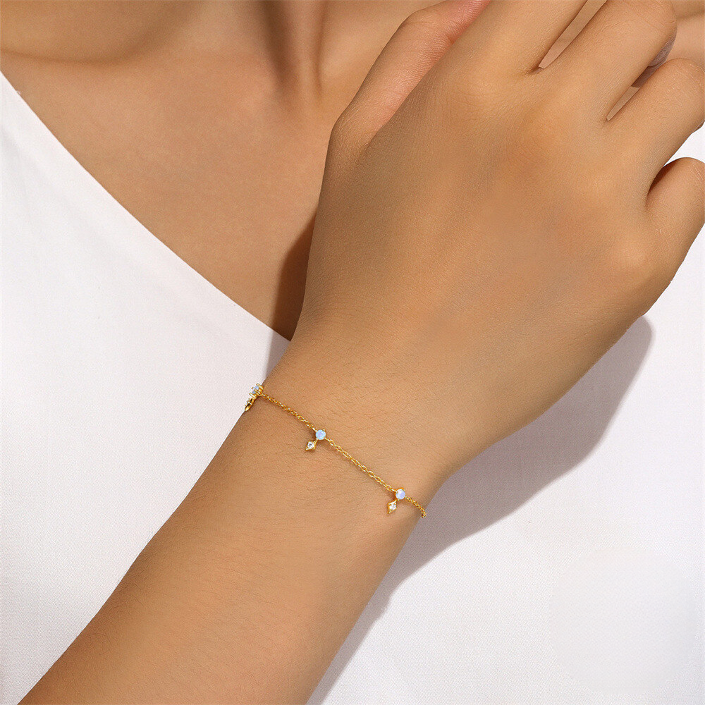 Gold bracelet with small stones on a wrist against a white background