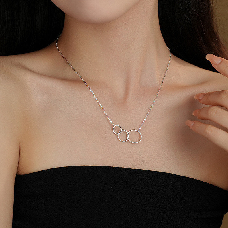 Silver necklace with interlocking rings worn by a person against a neutral background