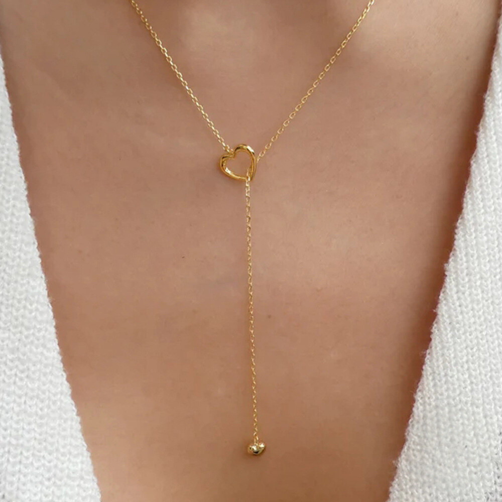 Gold necklace with a heart-shaped clasp on a person wearing a white garment.
