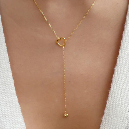 Gold necklace with a heart-shaped clasp on a person wearing a white garment.