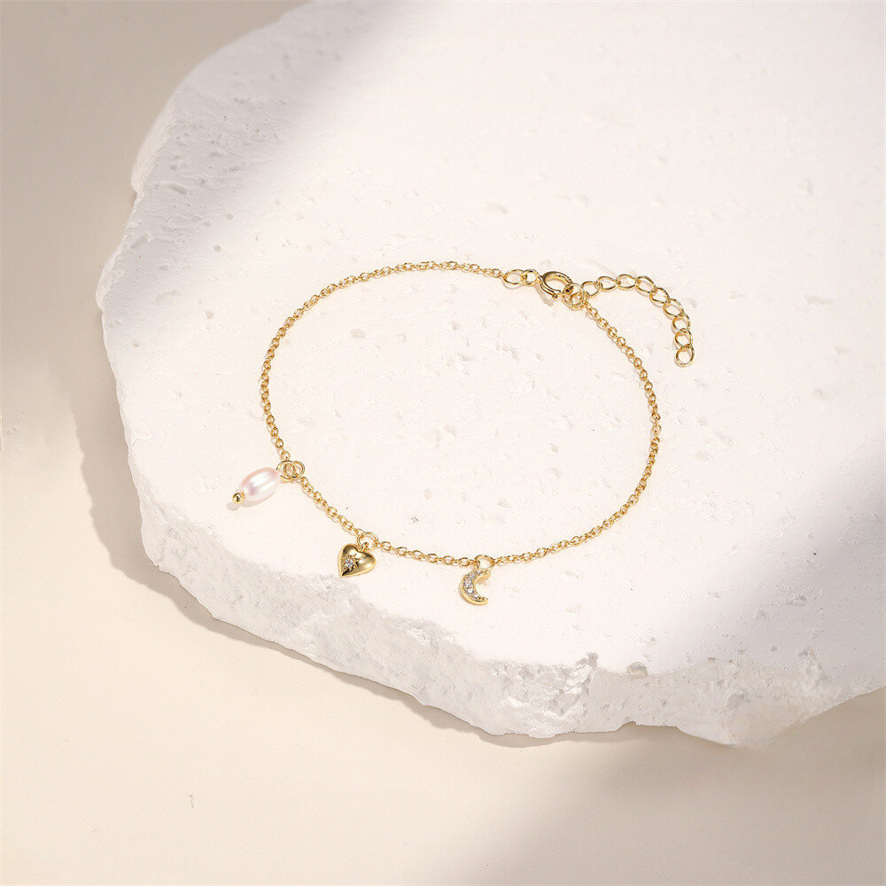 Gold bracelet with heart and moon charms on a white stone surface