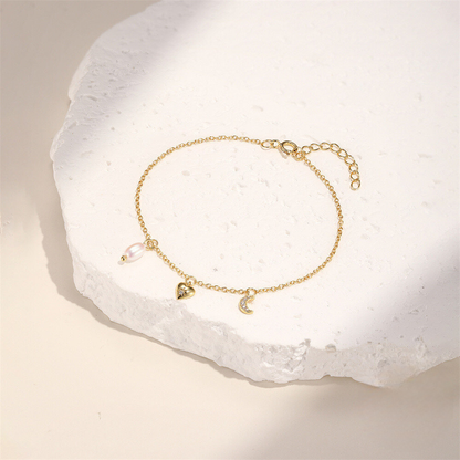 Gold bracelet with heart and moon charms on a white stone surface