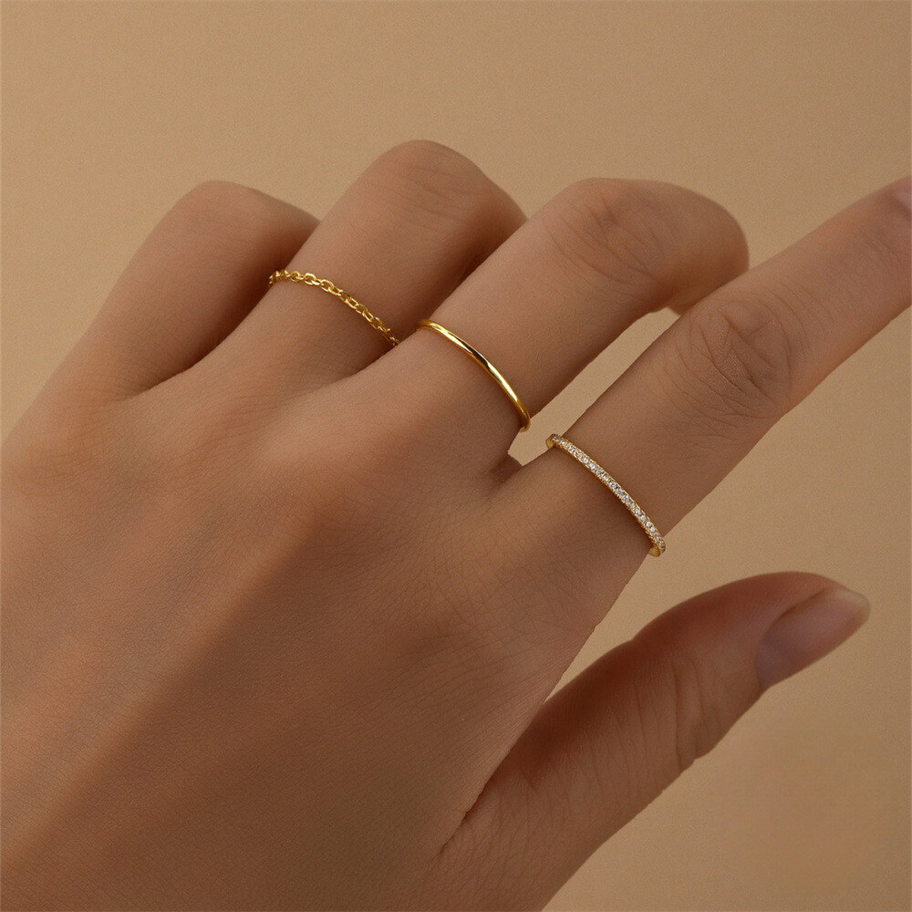 Hand wearing three gold rings on a beige background