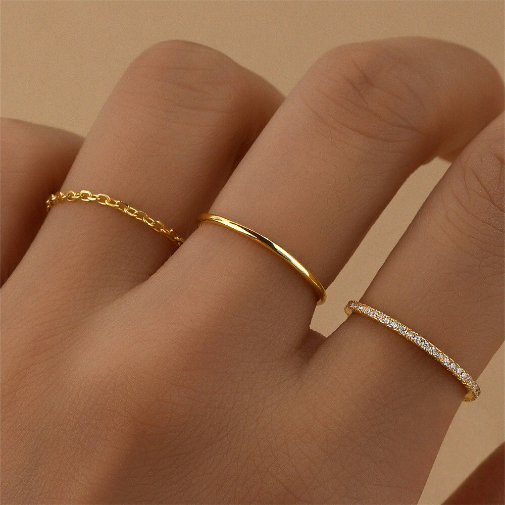 Three gold rings on a person's finger against a beige background