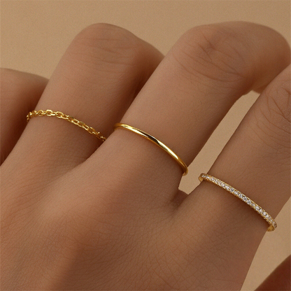Three gold rings on a person's finger against a beige background