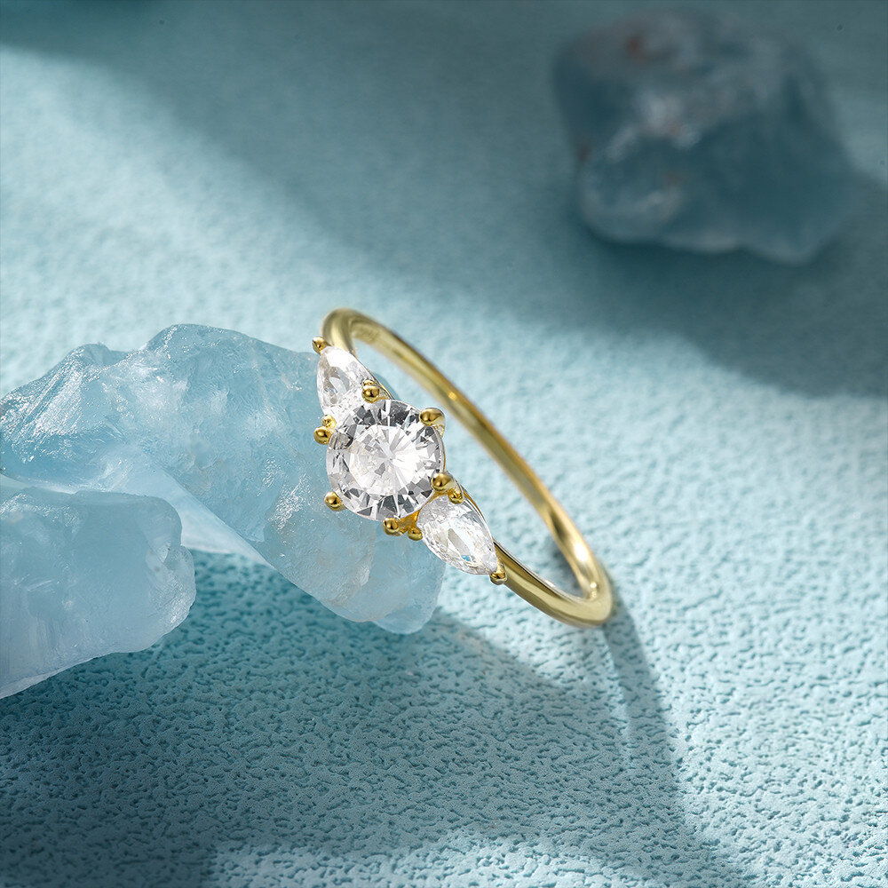 Gold ring with three clear gemstones on a light blue textured background