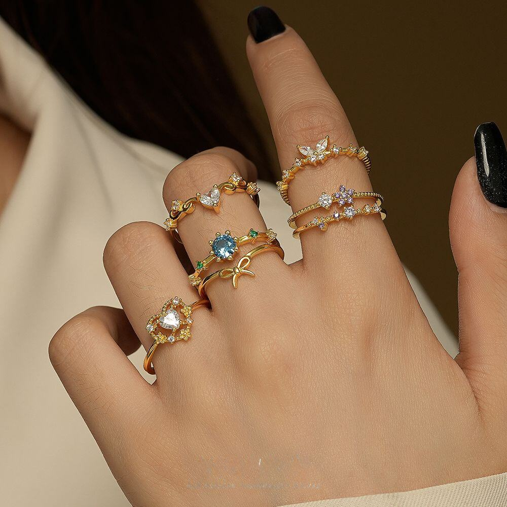 Hand wearing multiple gold rings with gemstones on a neutral background