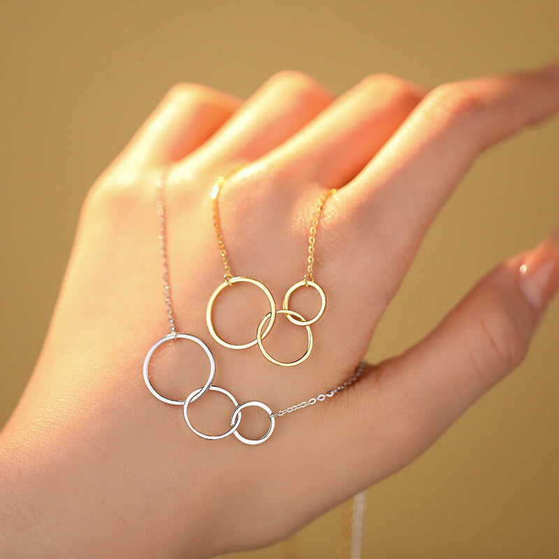 Gold and silver circular necklaces on a hand against a beige background