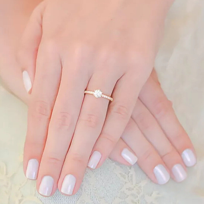 Hand wearing a gold ring with a diamond on a soft background