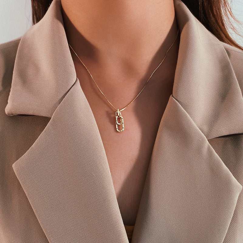 Necklace with a gold pendant worn by a person in a beige coat.