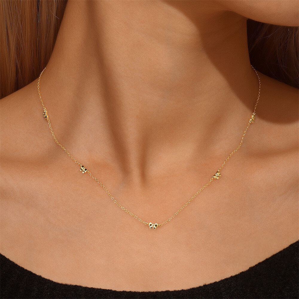 Gold necklace with small green pendants on a person wearing a black top.