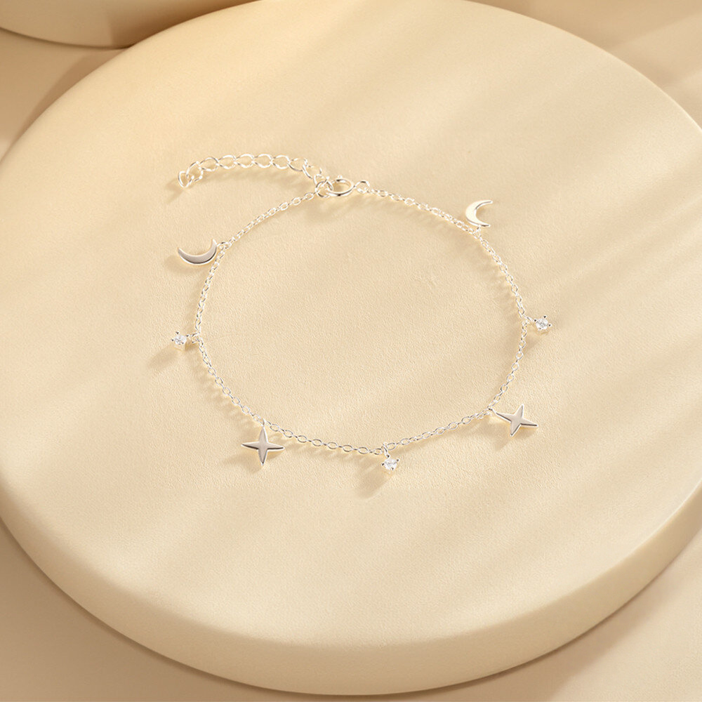 Silver bracelet with star and moon charms on a beige surface