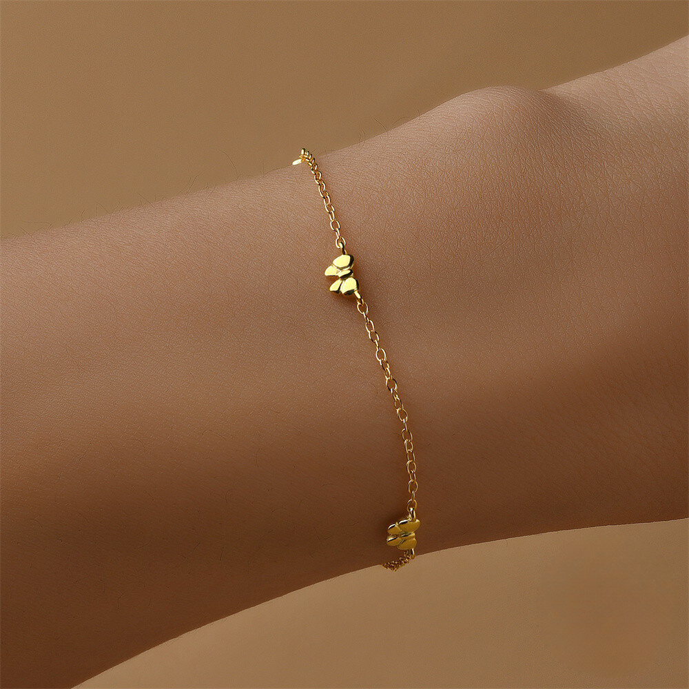 Gold bracelet with floral charms on a wrist against a beige background