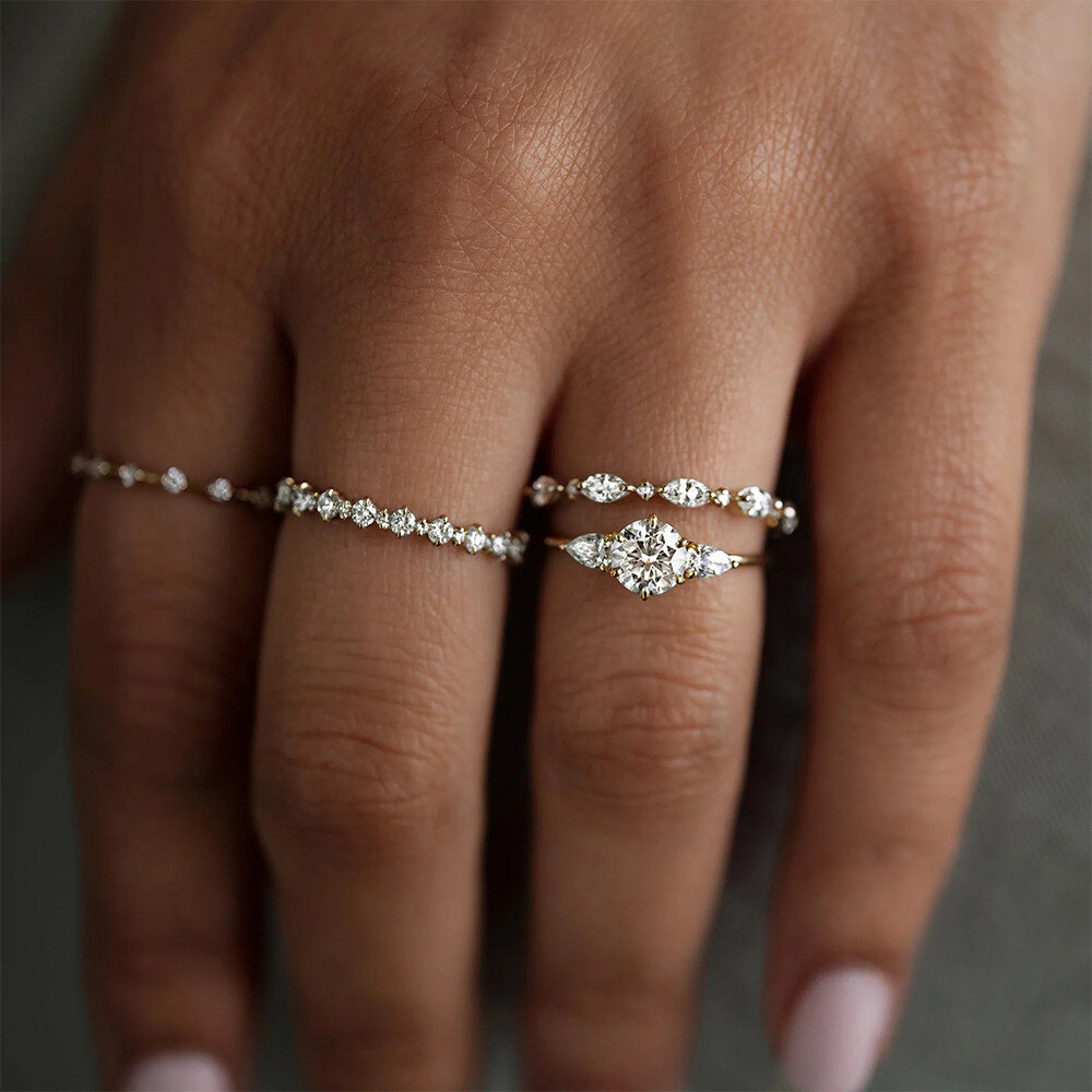 Close-up of a hand wearing two diamond rings on a neutral background