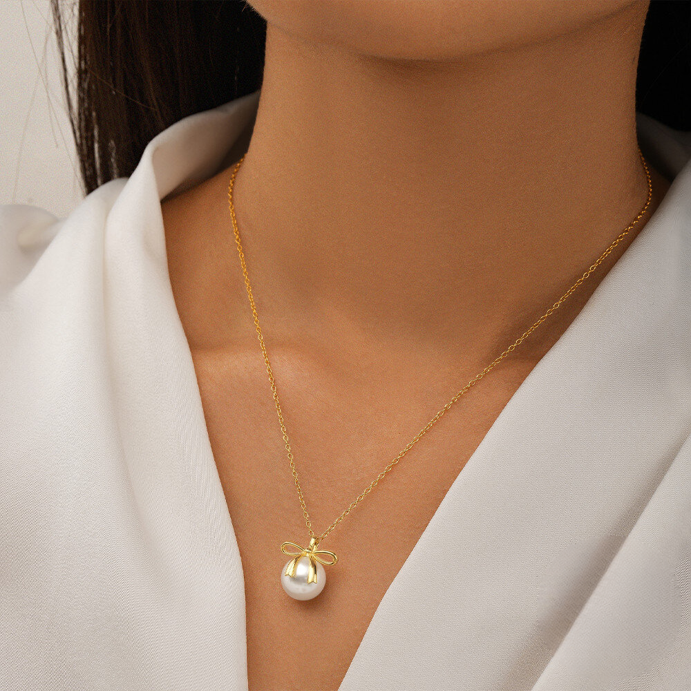 Gold necklace with a pearl pendant worn by a person in a white outfit.