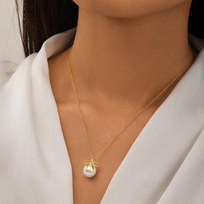 Gold necklace with a pearl pendant worn by a person in a white outfit.