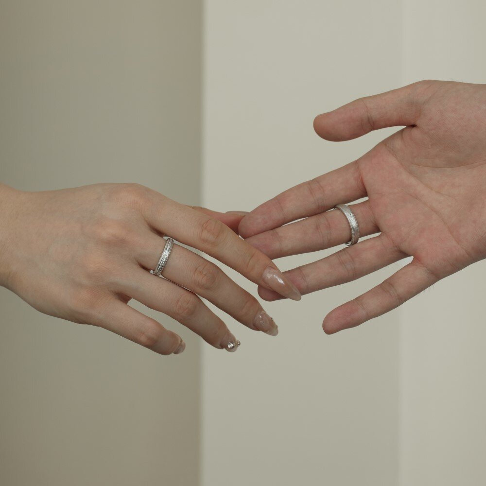 Two hands with silver rings on a neutral background