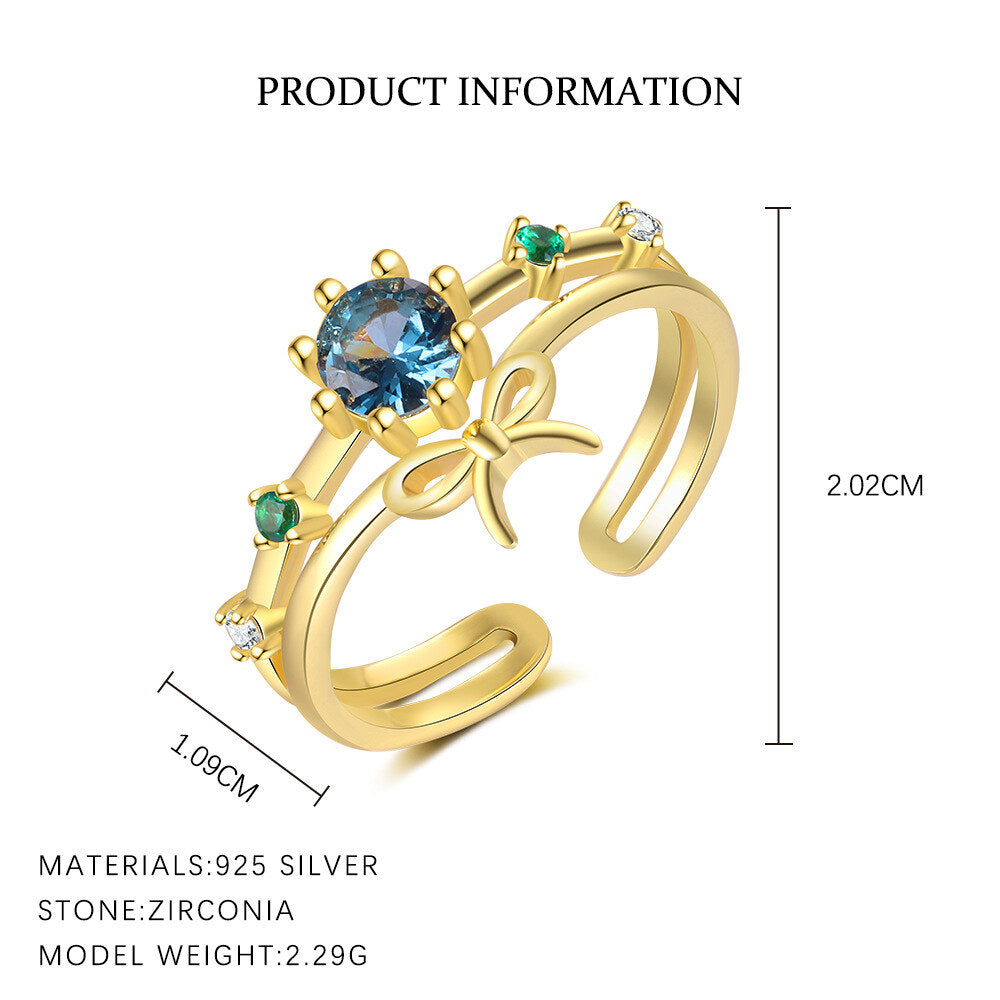 Gold ring with blue gemstone and green stones, featuring measurements and material details.