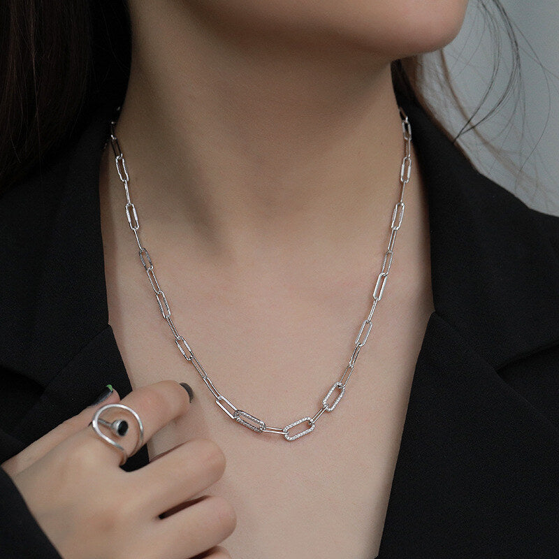 Silver chain necklace worn by a person against a dark background