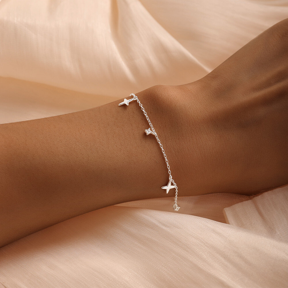 Silver bracelet with star-shaped charms on a wrist against a beige fabric background