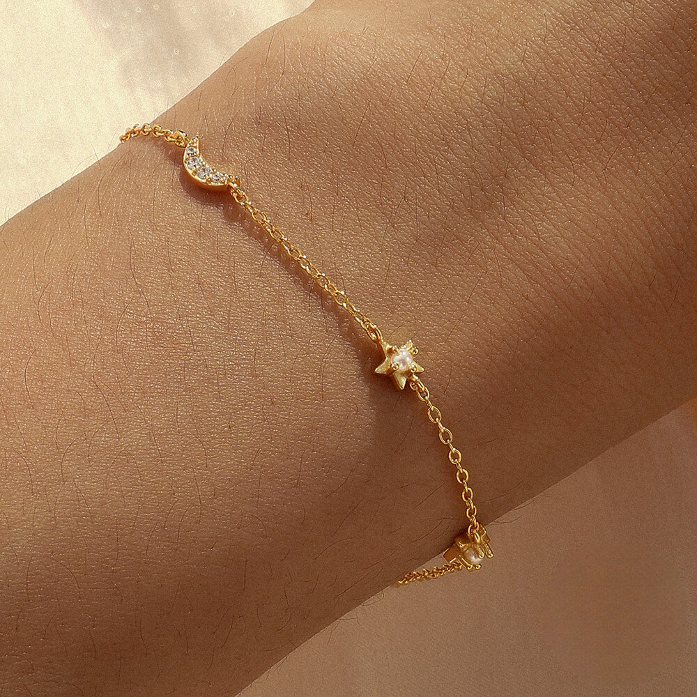 Gold bracelet with star and moon charms on a wrist against a beige background