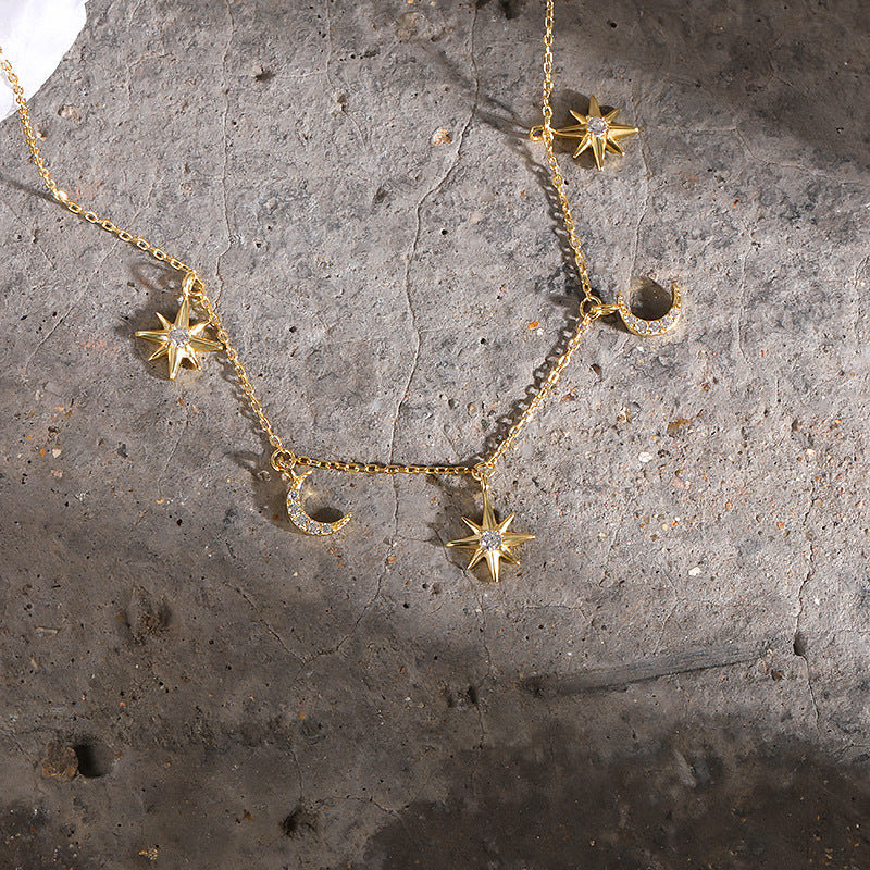 Gold necklace with star and moon pendants on a textured stone surface